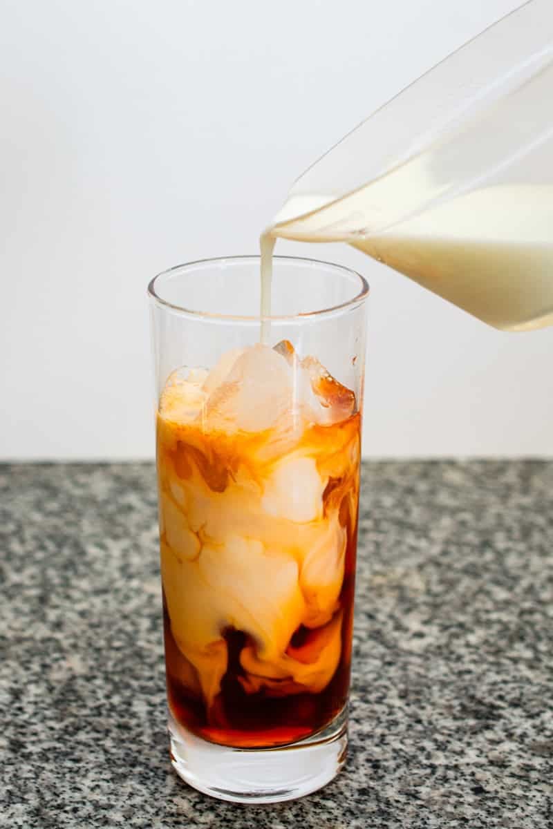pouring milk in a glass to make thai iced tea