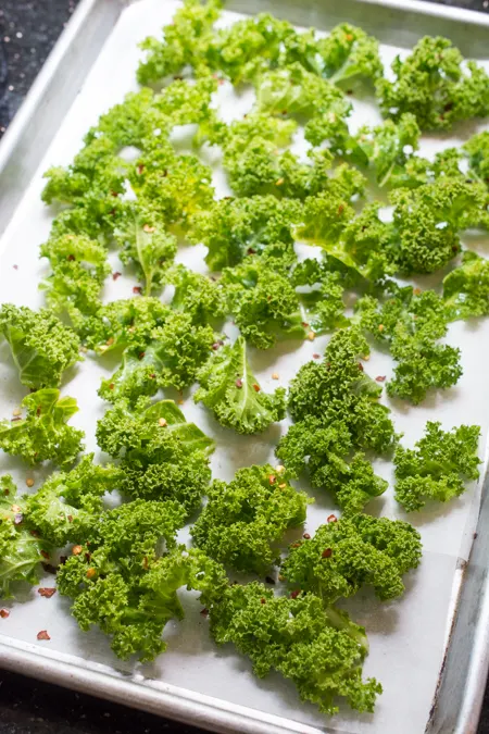 These healthy Spicy Garlic Kale Chips are irresistibly crispy and tasty! Fresh kale leaves are tossed in garlic oil and garlic powder, baked till crisp, then topped with crunchy garlic chips and spicy crushed red pepper. 