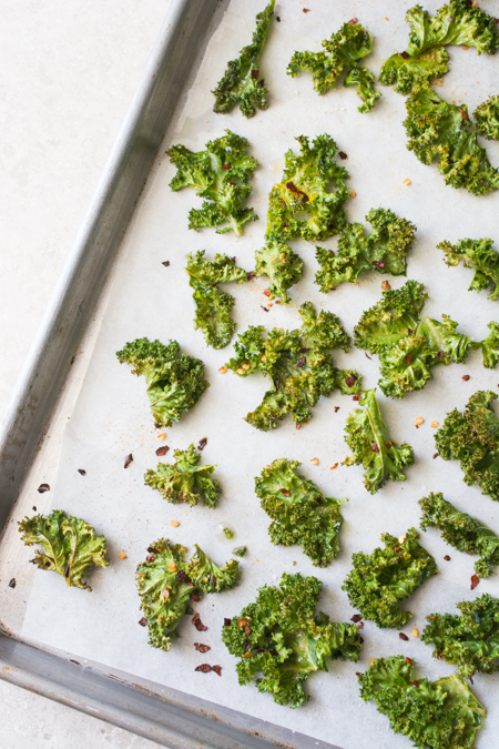 These healthy Spicy Garlic Kale Chips are irresistibly crispy and tasty! Fresh kale leaves are tossed in garlic oil and garlic powder, baked till crisp, then topped with crunchy garlic chips and spicy crushed red pepper. 