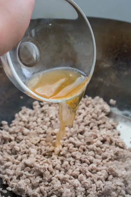 fish sauce being poured into ground pork for Thai Larb