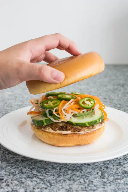 putting the burger bun on top of Vietnamese Lemongrass Pork Banh Mi Burger