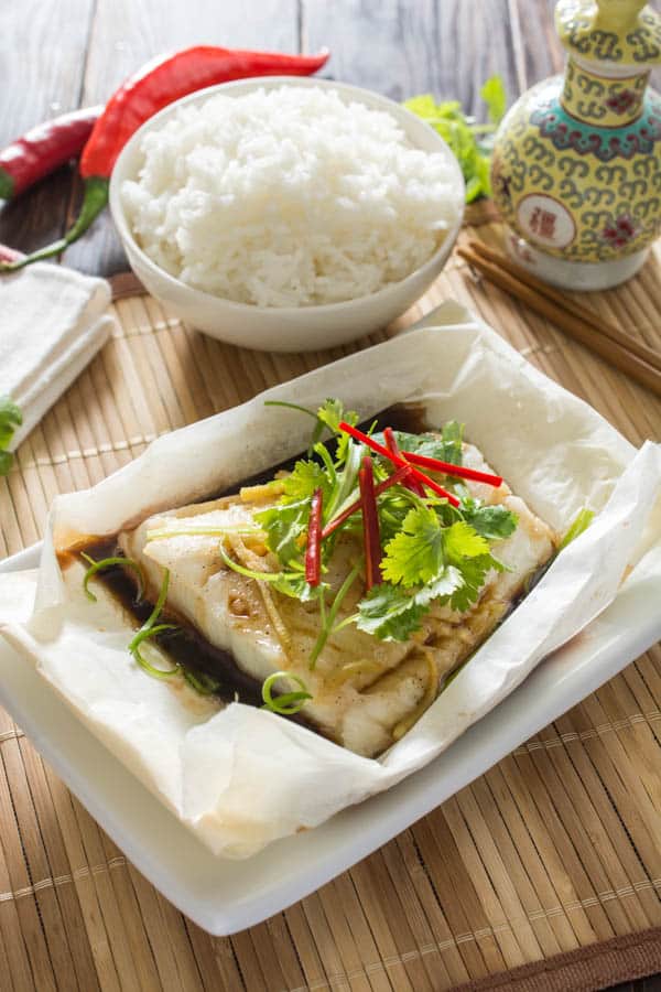 baked fish topped with scallions and red chili on parchment paper