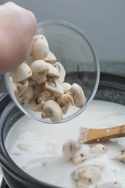 pouring mushrooms into tom kha gai soup