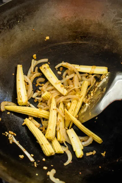 baby corn and sliced onion in a wok