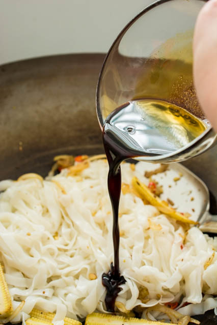 pouring sauce over pad kee mao noodles