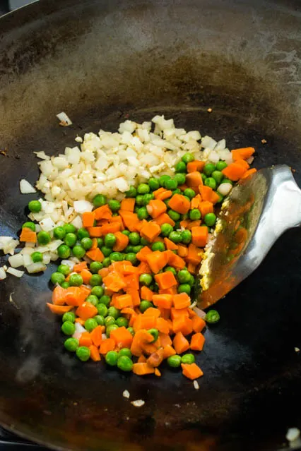 peas and carrots in wok with chopped onions