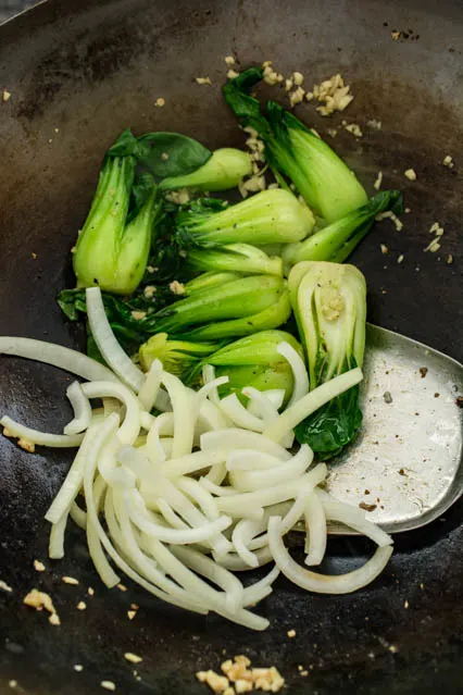 baby bok choy and onion slices in a wok