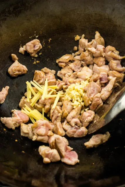 stir frying chicken, garlic and ginger in a wok for cashew chicken