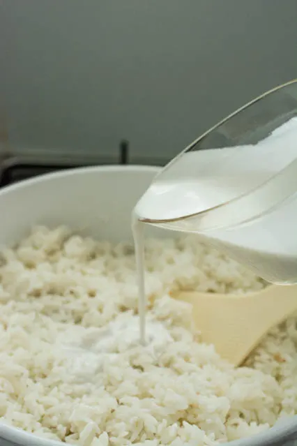 pouring coconut milk over nasi lemak
