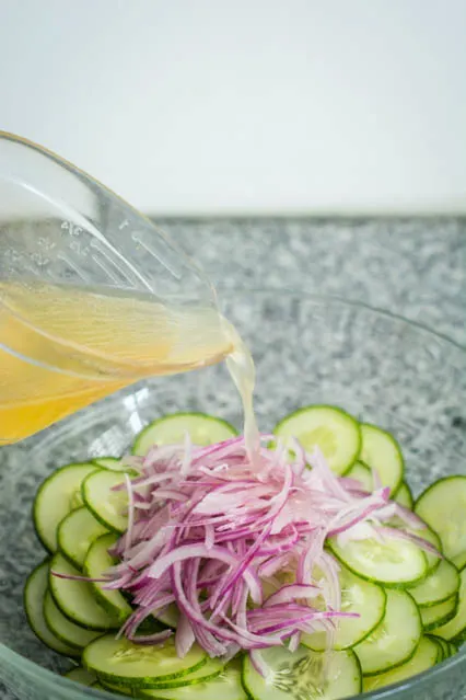 pouring dressing over thai cucumber salad