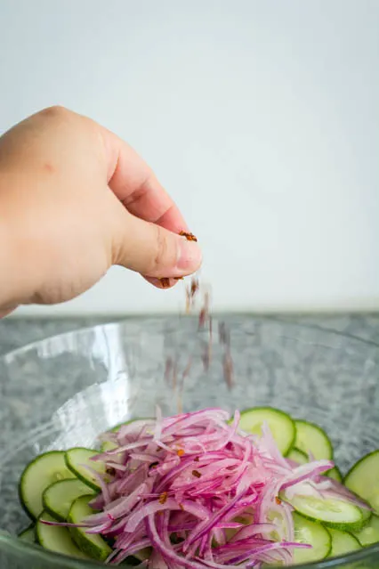 sprinkling crushed red pepper on thai cucumber salad