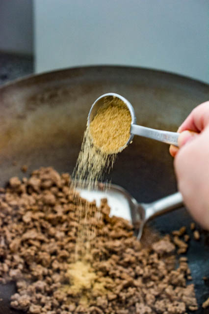 pouring brown sugar over ground beef for Korean Beef Bowls