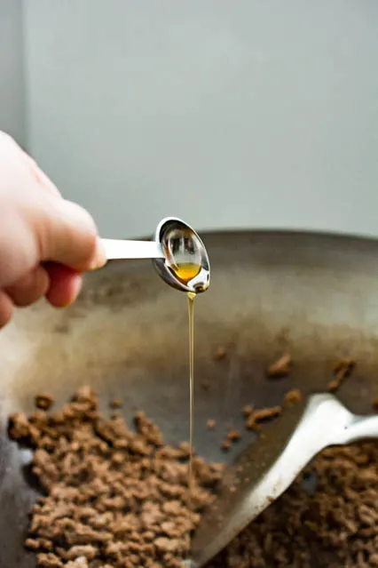 pouring sesame oil over ground beef in wok
