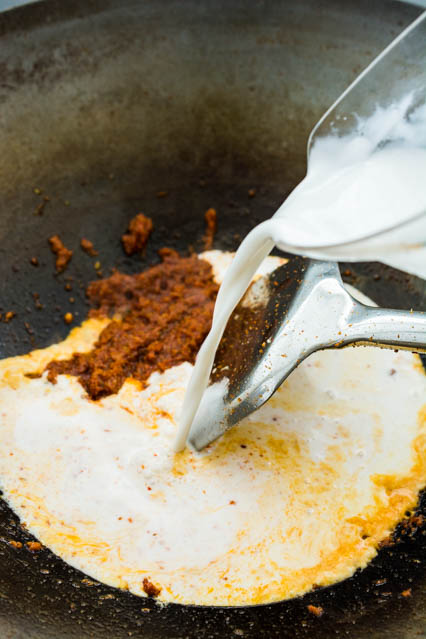 pouring coconut milk over thai red curry paste