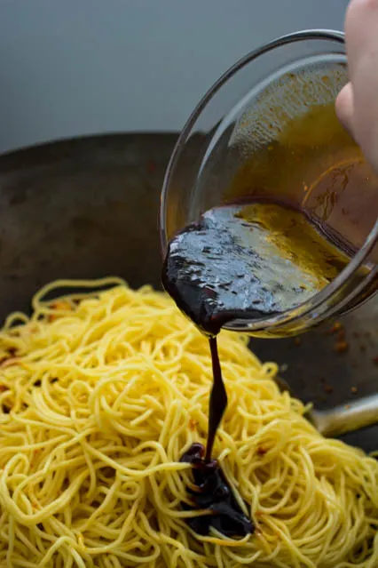 pouring kicap manis over yellow noodles