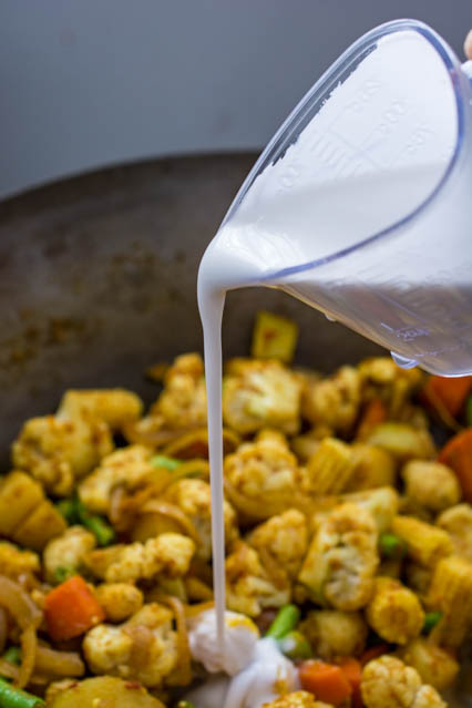 pouring coconut milk into wok over vegetables