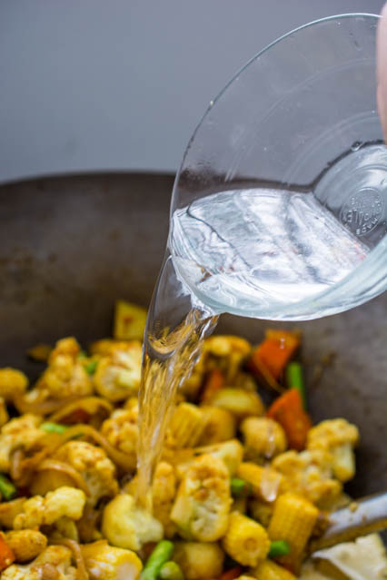 pouring water over vegetables in a wok