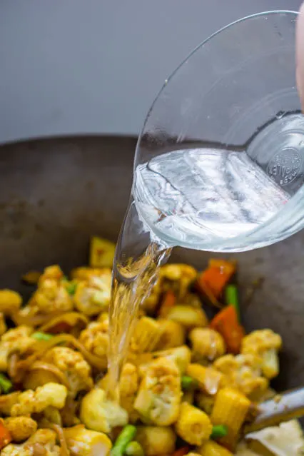 pouring water over vegetables in a wok