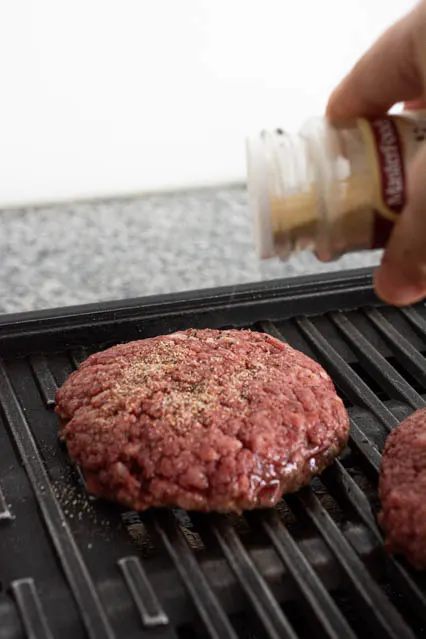 adding garlic powder to beef patty on grill