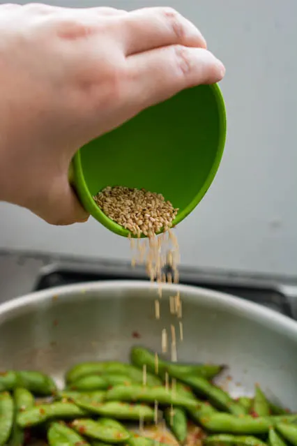 pouring toasted sesame seeds over edamame