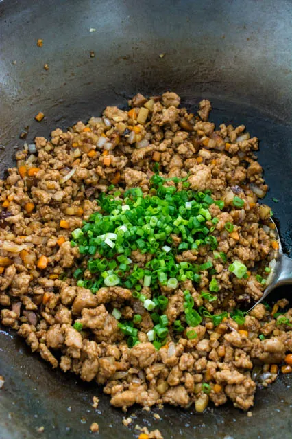 ground pork mixture with chopped scallions in wok