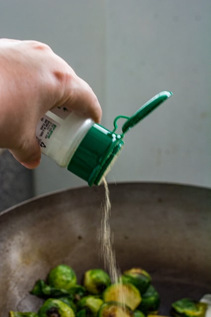 pouring garlic powder over stir-fried brussels sprouts