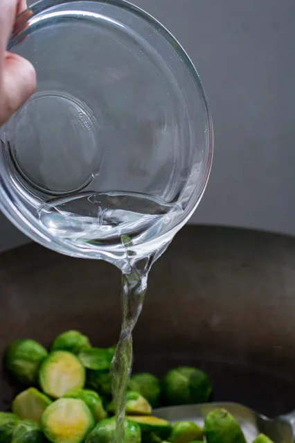 pouring water over brussels sprouts in a wok
