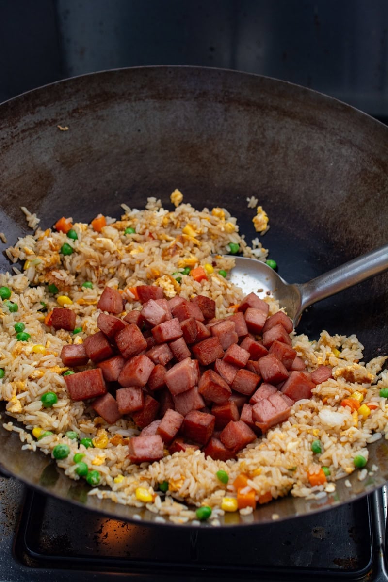 adding spam to fried rice in a wok