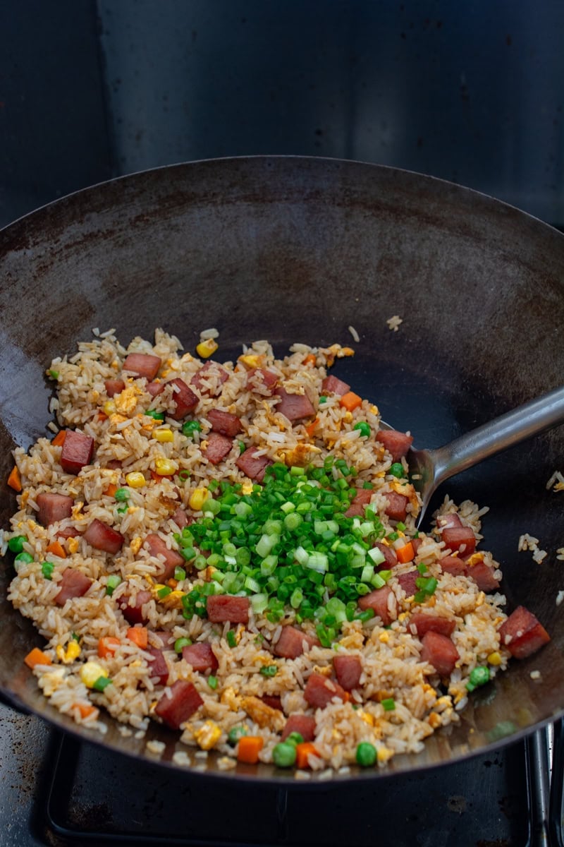 adding scallions to spam fried rice in a wok