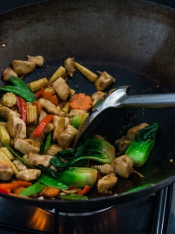 Colorful stir fry vegetables cooking in a wok with a spatula.