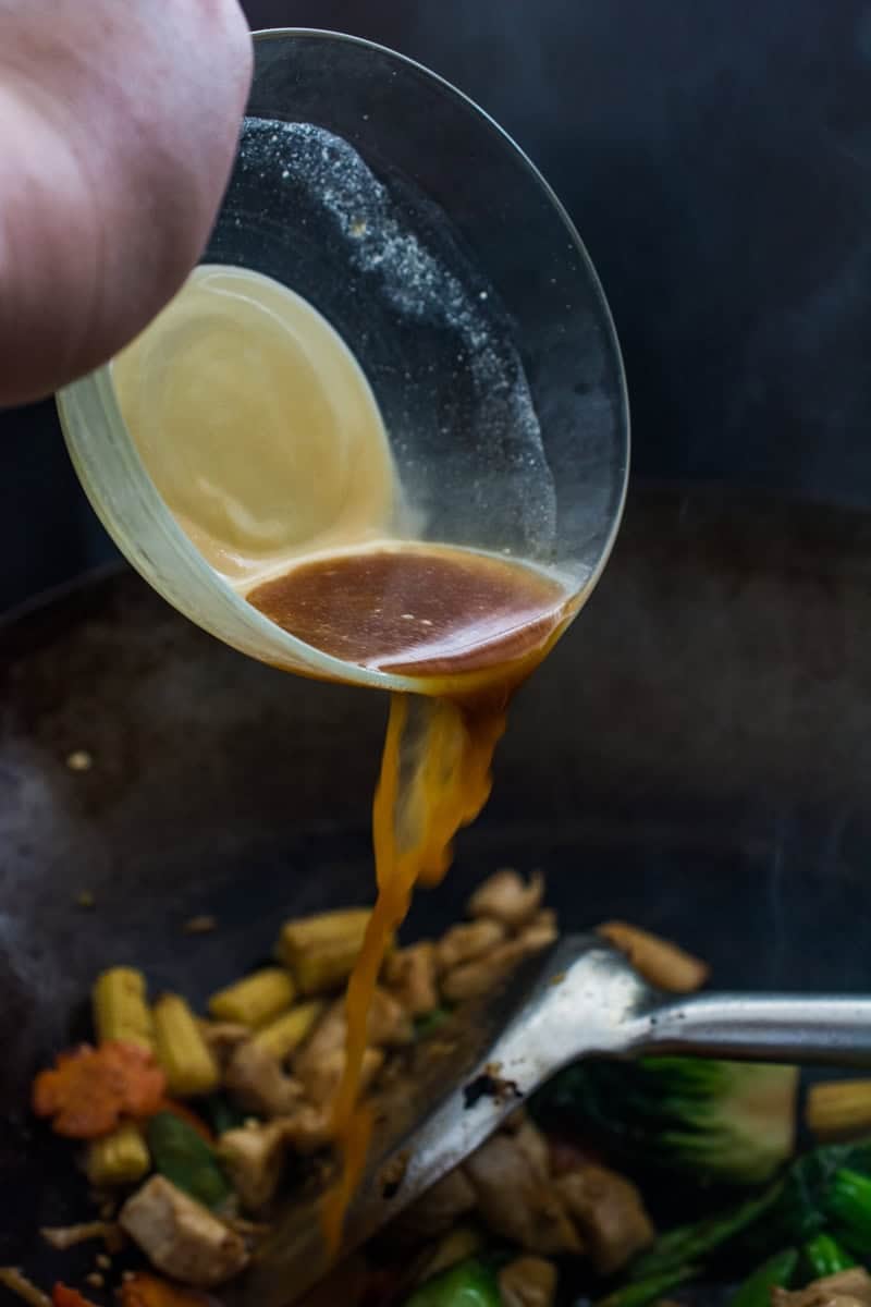 pouring sauce over stir fry in a wok